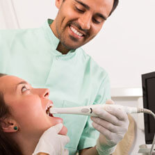a woman sits in a dental chair as the dentist uses an intraoral camera in her mouth