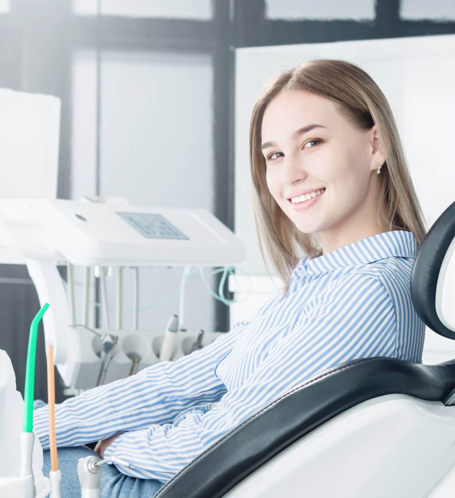 woman sitting in a dental chair turns to look at the camera and smiles